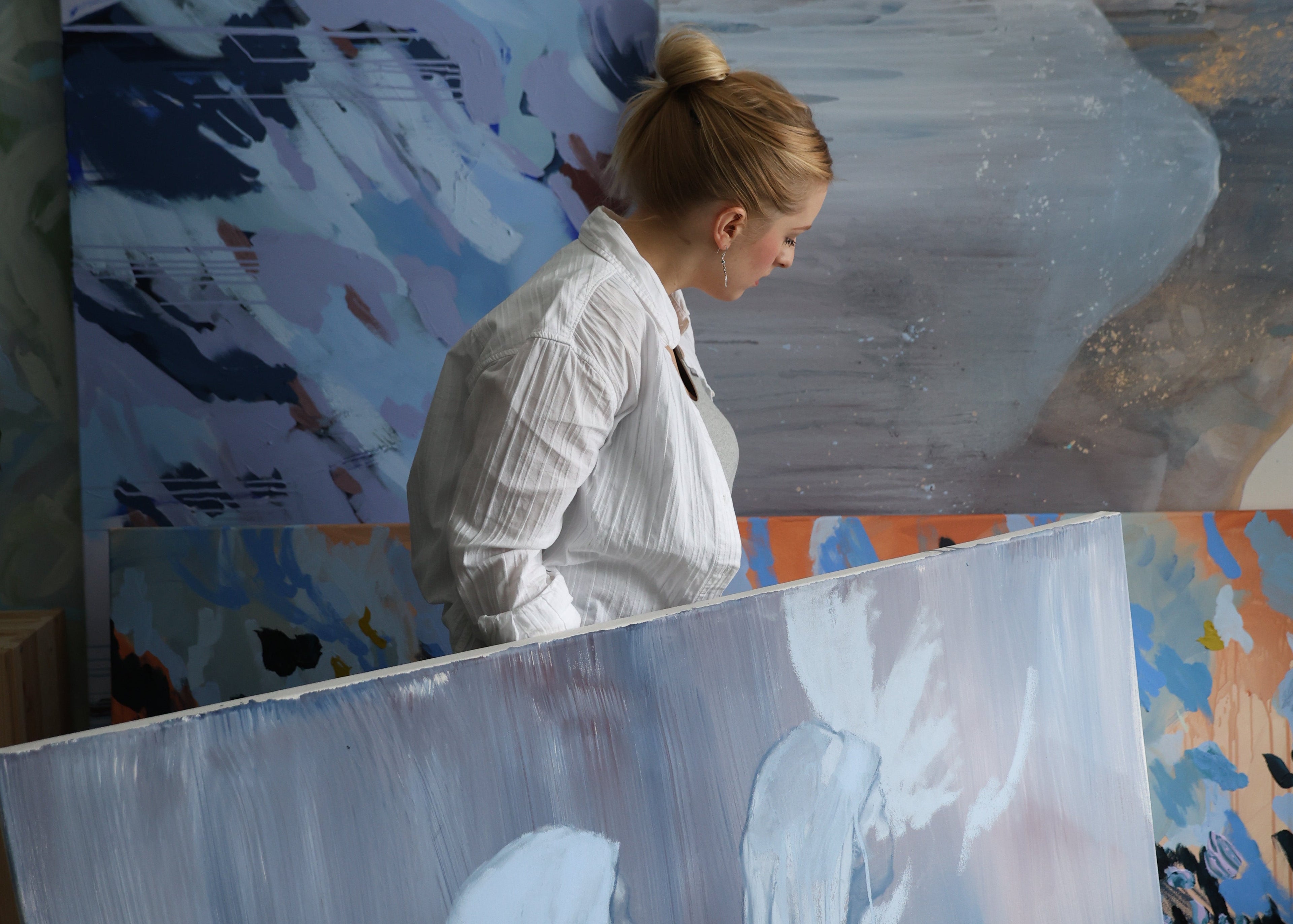 Person painting on a large canvas with abstract art in the background